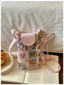 Vue détaillée du mini sac bandoulière rose brodé avec motifs floraux sur un livre ouvert