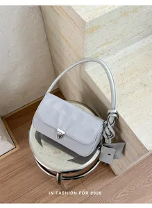 Borsa baguette grigio chiaro minimalista con mini pochette coordinata su uno sgabello.