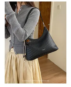 Dettaglio di un'elegante borsa sottobraccio tessuta nera con nappa.