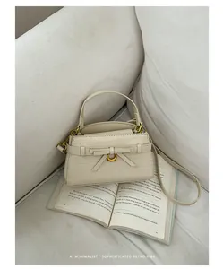 Elegante crèmekleurige handtas met steentextuur en strikdetail op een open boek