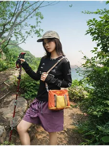 Asian model in hiking gear wearing a lightweight orange fabric crossbody tote bag outdoors.