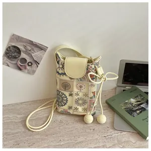 Vue détaillée d'un mini sac seau beige avec broderie florale complexe sur un bureau.