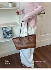 Donna che indossa una grande borsa tote intrecciata marrone in un interno elegante.