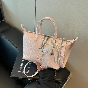 Detailed macro view of a pink woven tote bag featuring a pearl bow and chain charms