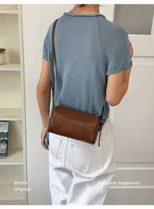 Back view of a model wearing a brown woven cylinder crossbody bag on a blue knit top