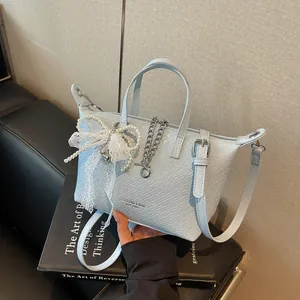 Detailed view of the light blue woven tote bag with a pearl bow and metal chain charm.