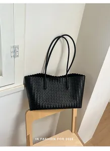 Grande borsa tote nera intrecciata su una sedia di legno minimalista in uno studio.
