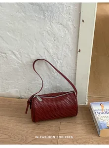 Detailed view of a retro burgundy woven barrel bag against a minimalist white wall backdrop.