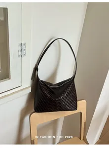 Dark brown woven underarm shoulder bag for women resting on a minimalist wooden chair