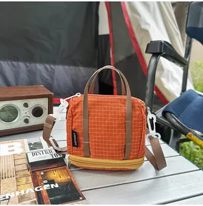 Small orange grid crossbody bag displayed on a silver camping table in a tent setting