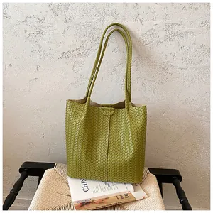 Dettaglio ravvicinato di una borsa tote verde intrecciata posata su libri e una sedia