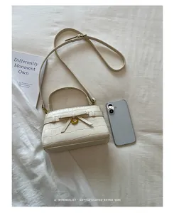 Elegante crème handtas met krokodillenpatroon en strik naast een smartphone display