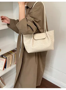 Detail shot of cream woven tote bag styled with a classic brown trench coat and books