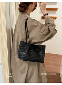 Elegant black woven leather tote bag worn as a shoulder bag in a stylish lifestyle setting