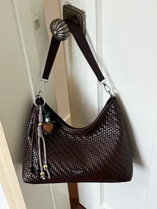 Elegante borsa a spalla intrecciata marrone scuro con nappa decorativa appesa a una porta.