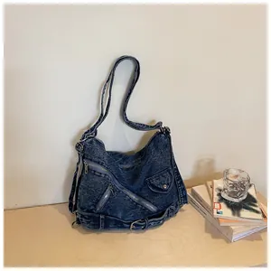 Große blaue Denim-Schultertasche im Motorrad-Stil mit Reißverschlüssen auf einem Holztisch
