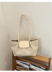 Detailed view of a cream woven tote bag with flap closure placed on a wooden shelf.