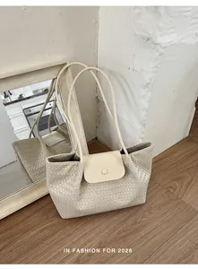 Macro view of cream woven underarm bag featuring a magnetic flap and long straps