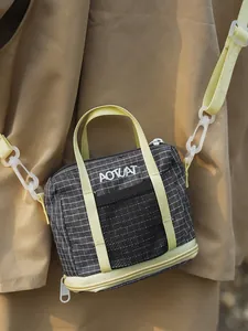 Casual black grid small crossbody bag with vibrant yellow straps worn by a model