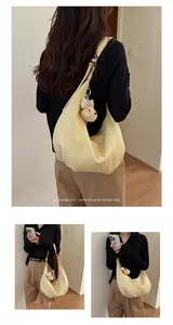 Detail view of a minimalist creamy yellow pleated hobo bag with a bear charm