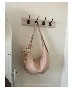 Close-up of a minimalist pink ruched hobo bag hanging on a hook with bear charm.