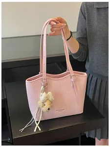 Close-up detail view of a pink textured shoulder tote bag featuring a cute plush bear charm