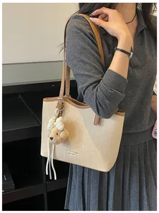 Large beige woven tote bag with brown trim and cute teddy bear charm for daily work.