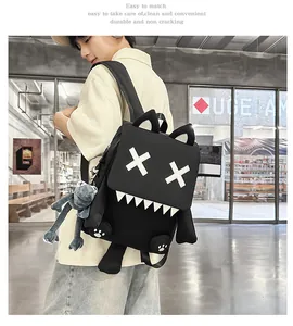 Trendy black cartoon monster backpack with X eyes and plush frog keychain on model