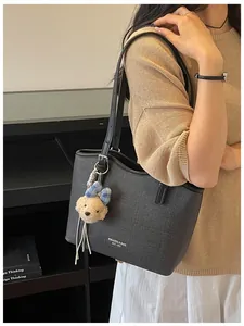 Detailed shot of a black cross-textured tote bag with a dog charm worn by a model