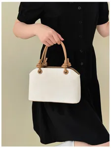 Detail einer eleganten weißen Handtasche mit braunen Knotengriffen und schwarzem Kleid.