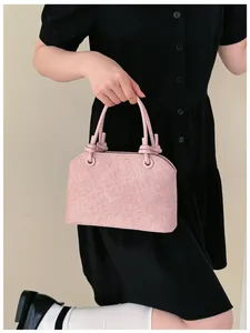 Détail d'un sac à main rose texturé avec poignées nouées sur fond de robe noire.