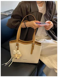Stylish beige textured tote bag with wavy rim, brown leather straps, and cute bear charm