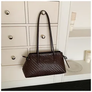 Bolso Boston trenzado marrón oscuro colgado del pomo de un mueble blanco de estilo retro.