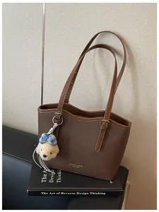 Detailed view of a brown textured leather tote bag with a cute bear charm on a black book.