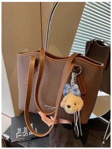 Close-up of brown textured tote bag with cute bear charm and thin shoulder straps