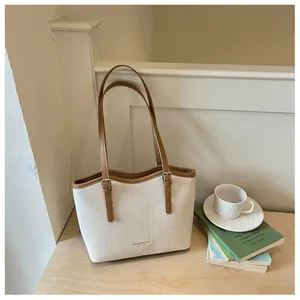 Detail view of a cream canvas tote bag with brown leather straps in a lifestyle setting