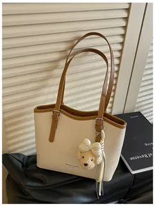 Detail of a chic beige woven tote bag with brown leather straps and bear charm