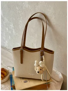 Close-up of cream woven tote bag featuring brown straps and a cute teddy bear charm