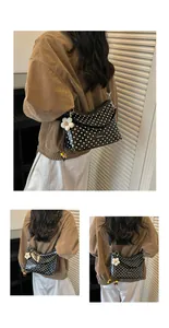 Black polka dot shoulder bag with white flower charm shown on model in detail view.