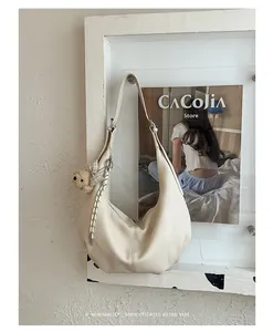 Detailed view of a cream pleated hobo bag with a cute bear charm hanging on a wall.