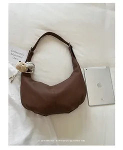 Detailed view of brown pleated retro hobo bag displayed on white textured bedding