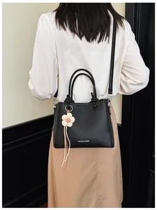 Elegante bolso de mano negro de piel sintética con colgante de flor, visto por detrás
