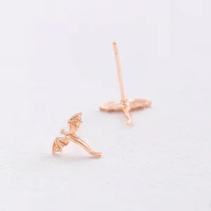 Detailed view of delicate rose gold flying dragon stud earrings on white paper