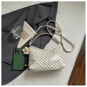 Detailed view of white polka dot shoulder bag with stylish floral charm accent