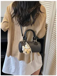 Back view of a model carrying a stylish black barrel bag with a cute plush bear charm