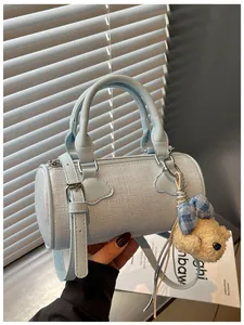 Detail view of a light blue textured barrel handbag with a cute teddy bear charm