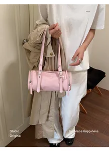 Detail of a vintage pink cylinder shoulder bag held by a model in a stylish indoor setting