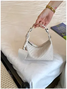 Elegant white woven dumpling handbag for women held by hand on a minimalist bed scene