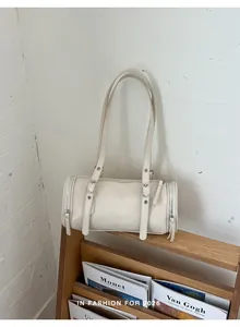 Elegant cream-colored minimalist cylinder shoulder bag displayed on a stylish wooden shelf