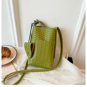Vue détaillée d'un mini sac de téléphone tissé vert sur un tissu texturé blanc.